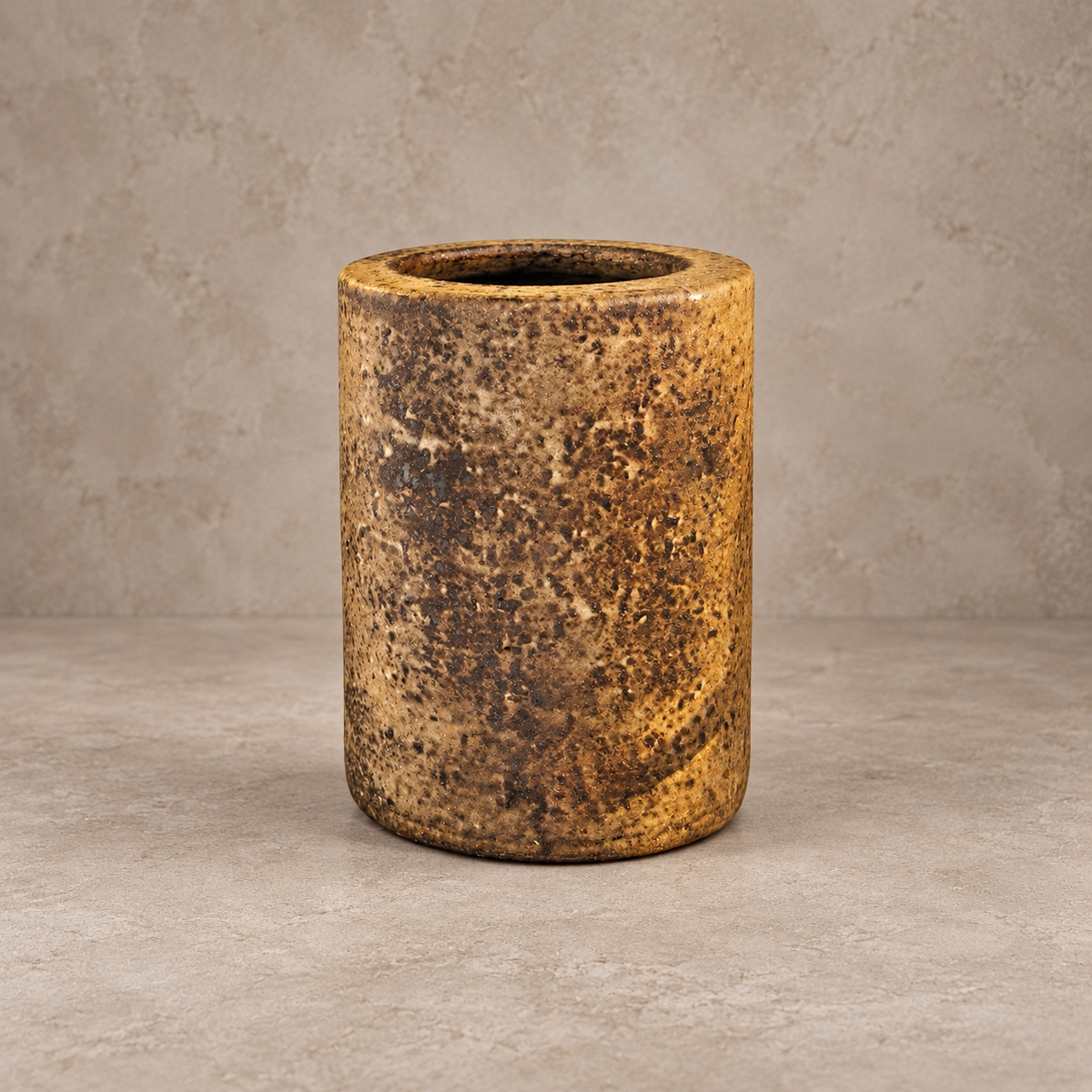 A cylindrical ceramic planter or vase with a rustic, textured glaze in earthy brown and gold tones, set against a neutral concrete-textured background.