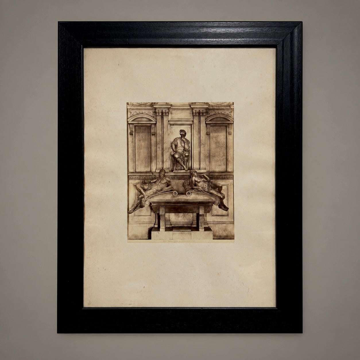 A framed sepia-toned architectural sketch or print mounted on a cream mat, enclosed in a black frame against a neutral gray wall.
