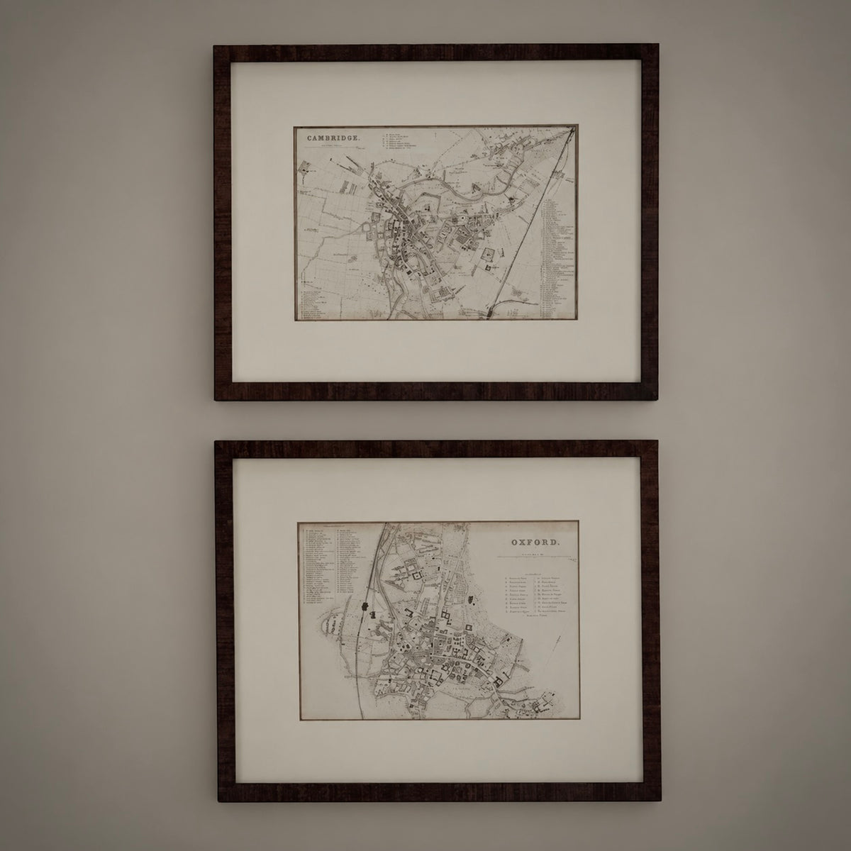 Two framed vintage maps of Oxford, England, displayed vertically on a neutral gray wall. Each map is housed in a dark brown wood frame with a white mat border.