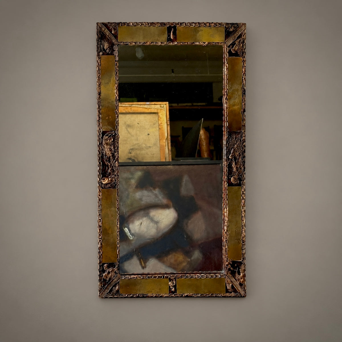 An antique metal-framed mirror with intricate detailing, displaying a reflective surface and an aged patina, placed against a neutral background.