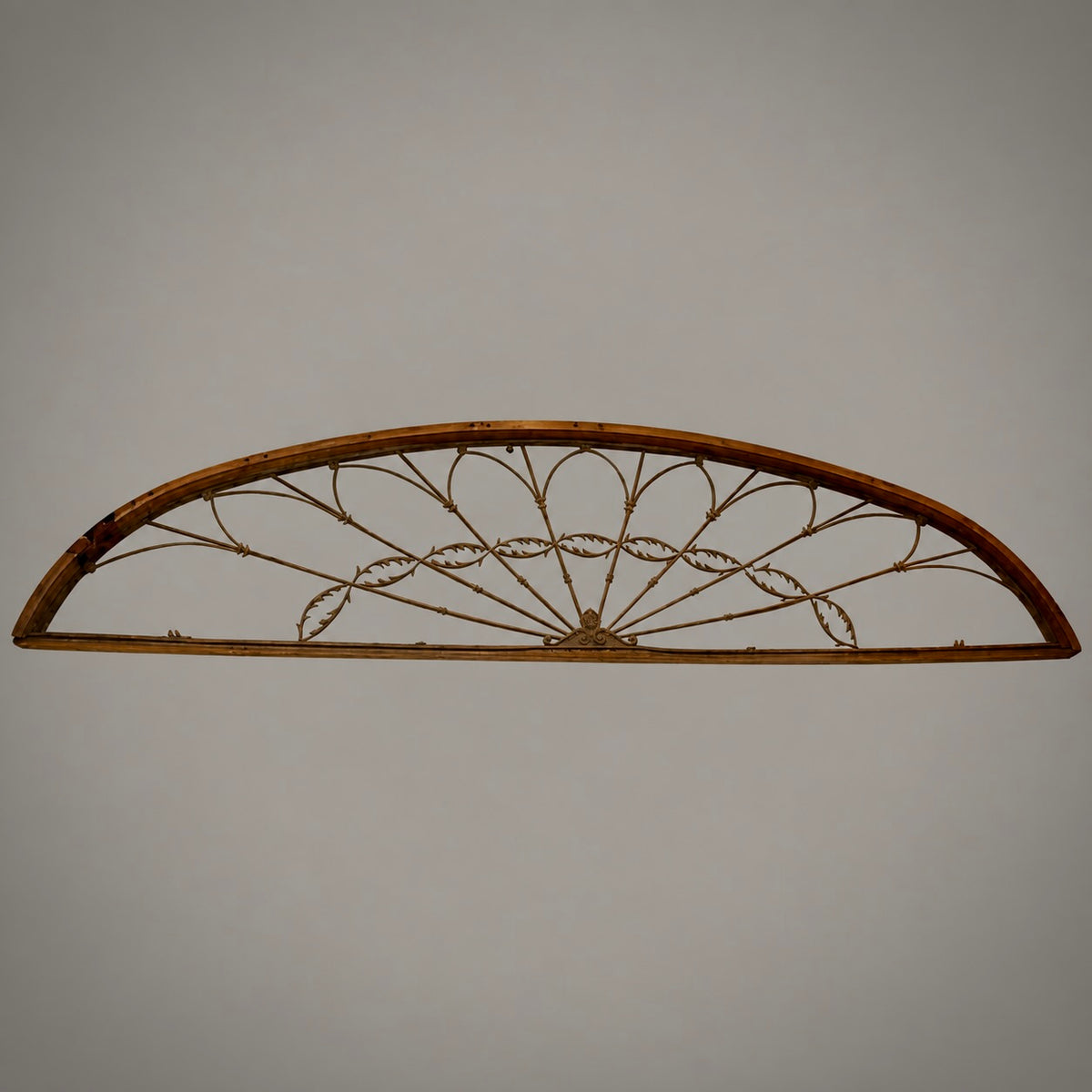 An antique metal fan-shaped window divider with a decorative wire fan pattern, mounted on a plain light gray background.
