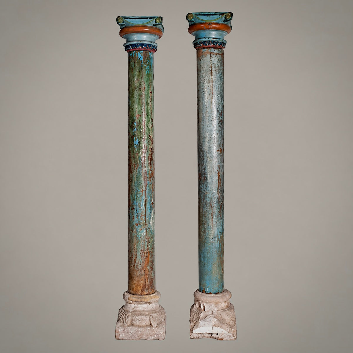 A pair of distressed, vintage-style classical column pedestals with peeling teal, green, and brown paint, set against a solid neutral gray background.