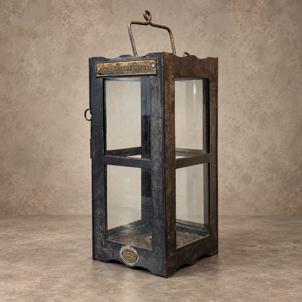 A vintage-style lantern with a distressed dark blue and brown wood finish, clear glass panels, and brass metal accents, set against a textured beige background.