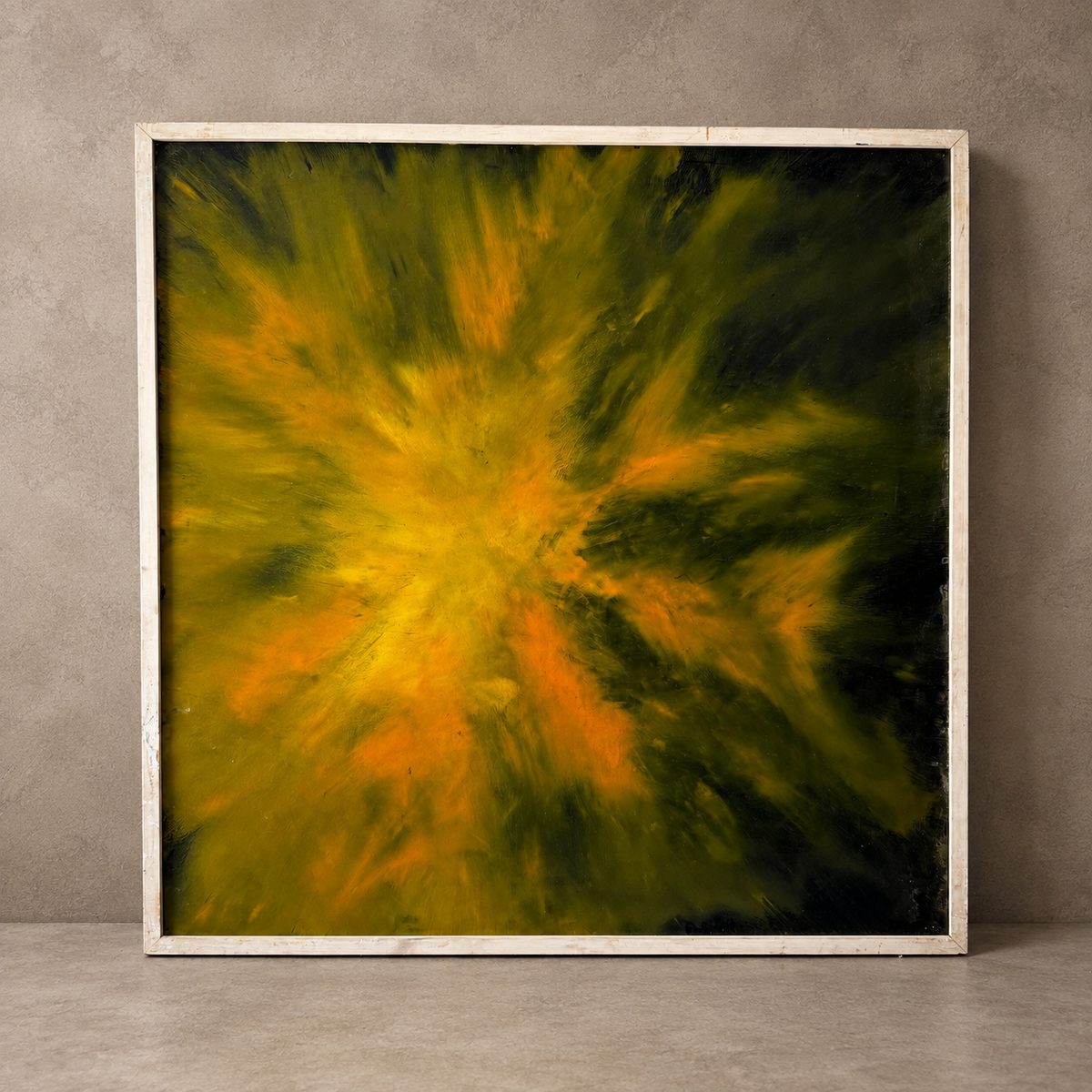 A square framed abstract painting featuring a vibrant yellow and orange burst radiating from the center against a dark background, displayed on a gray concrete floor against a textured gray wall.