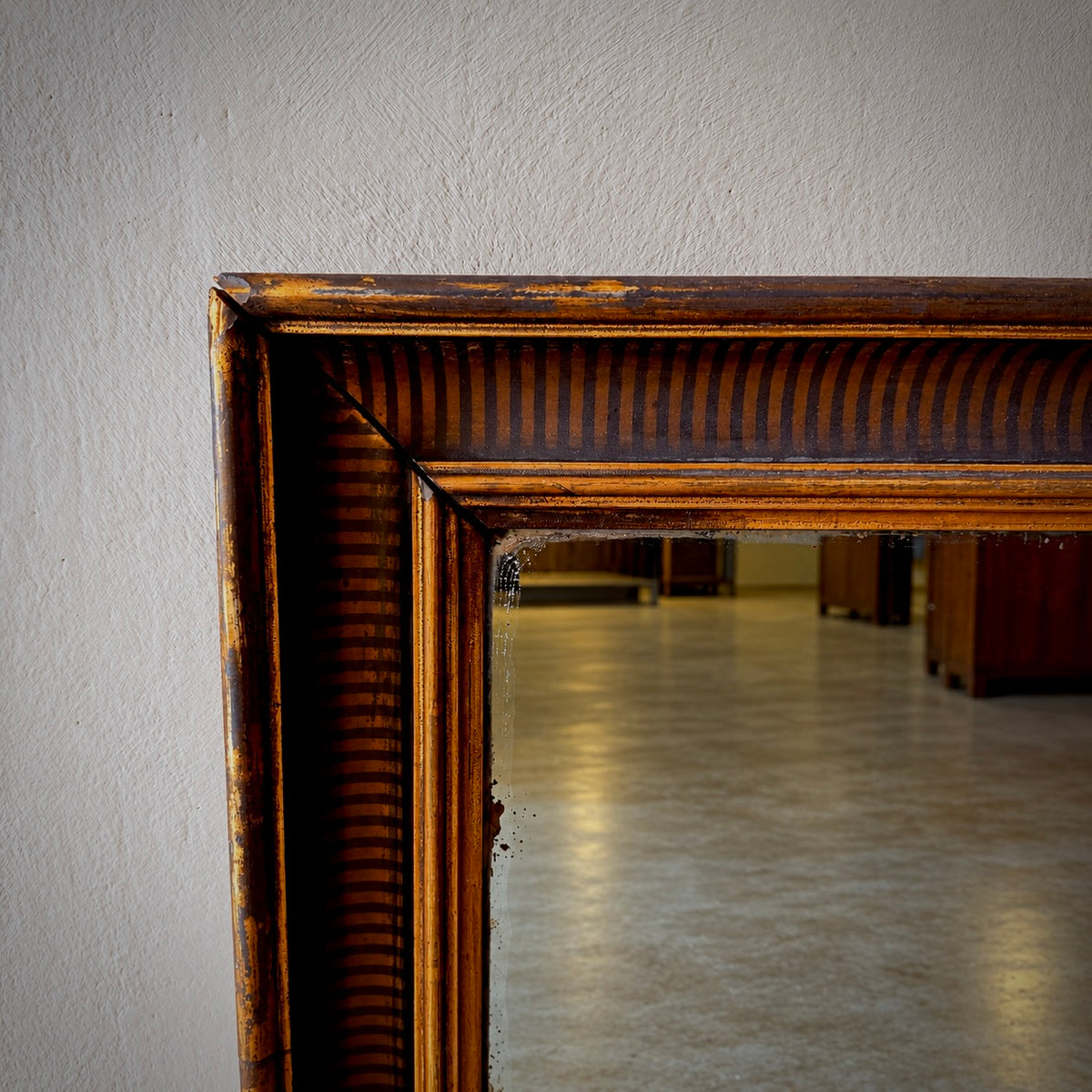 Close-up of a large antique-style mirror with a distressed dark brown wooden frame, showing a reflection of an empty room.