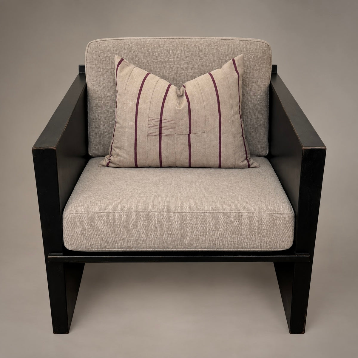 A modern outdoor armchair with a black frame and light beige textured cushions, featuring a matching striped accent pillow in beige with dark purple stripes.