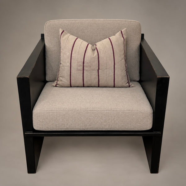 A modern outdoor armchair with a black frame and light beige textured cushions, featuring a matching striped accent pillow in beige with dark purple stripes.