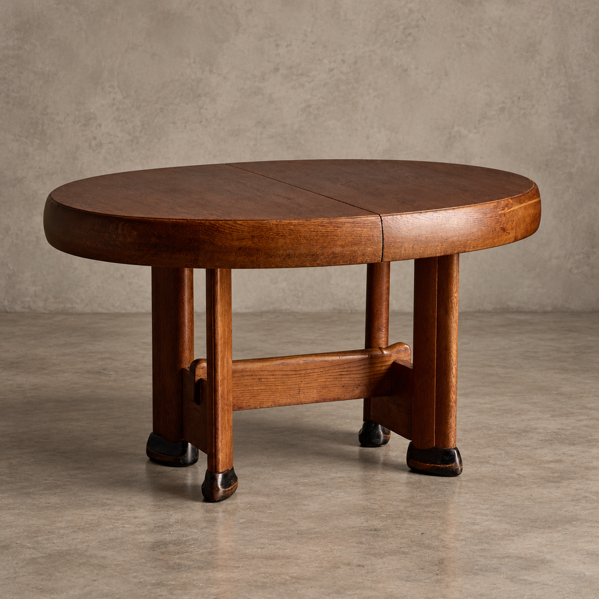A round wooden table with a warm medium-brown finish, featuring a central seam on the tabletop and a matching wooden stretcher base, set against a textured gray concrete wall and floor.