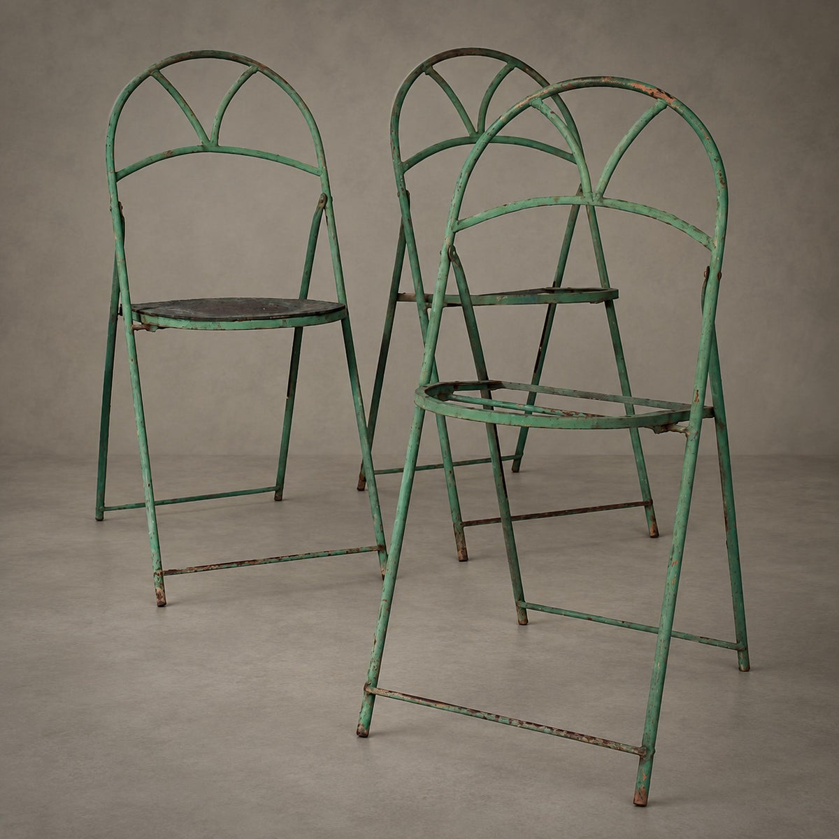 Three vintage green metal folding chairs with a distressed, weathered finish, arranged on a neutral gray studio background.