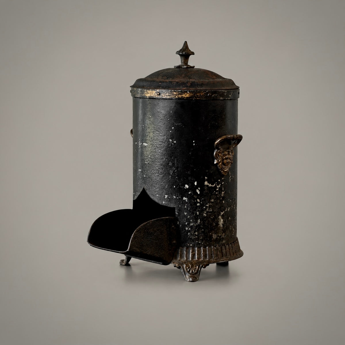An antique black cast iron chimney starter with a weathered, distressed finish and ornate gold-toned metal accents, shown on a neutral gray background.