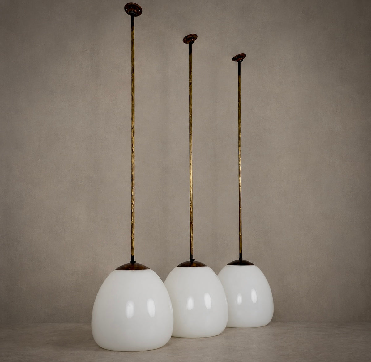 Three vintage-style pendant lights with white glass globes and long gold-toned metal rods, displayed against a neutral textured beige background.