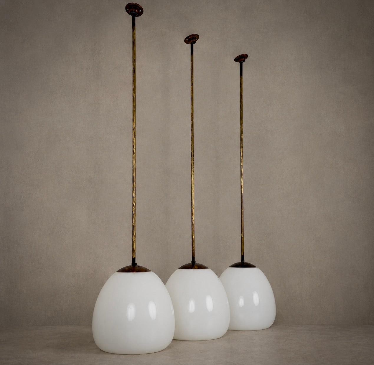 Three vintage-style pendant lights with white glass globes and long gold-toned metal rods, displayed against a neutral textured beige background.