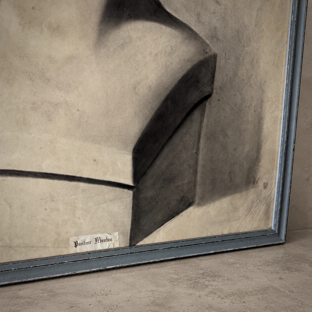 A framed abstract art print featuring a geometric composition of dark gray and black shapes on a textured beige background, set in a distressed blue-gray frame.