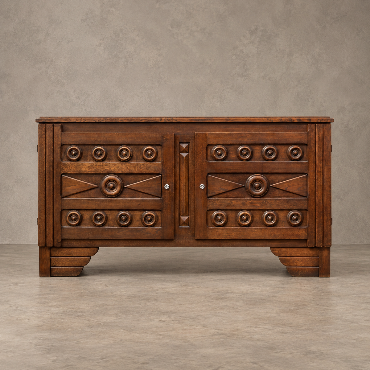 A rustic brown wooden sideboard with carved geometric details and circular metal knobs, set against a textured gray wall and concrete floor.