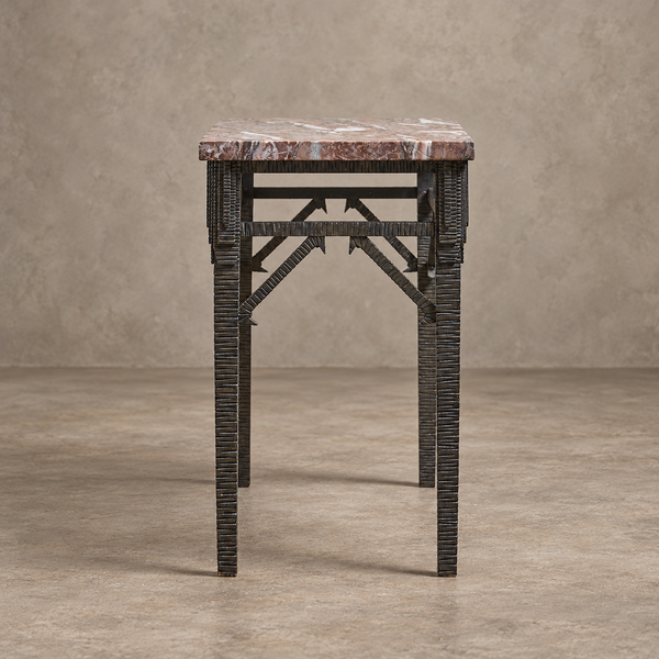 A small console table featuring a reddish-brown marble top and a dark, textured woven metal frame with geometric support beams.