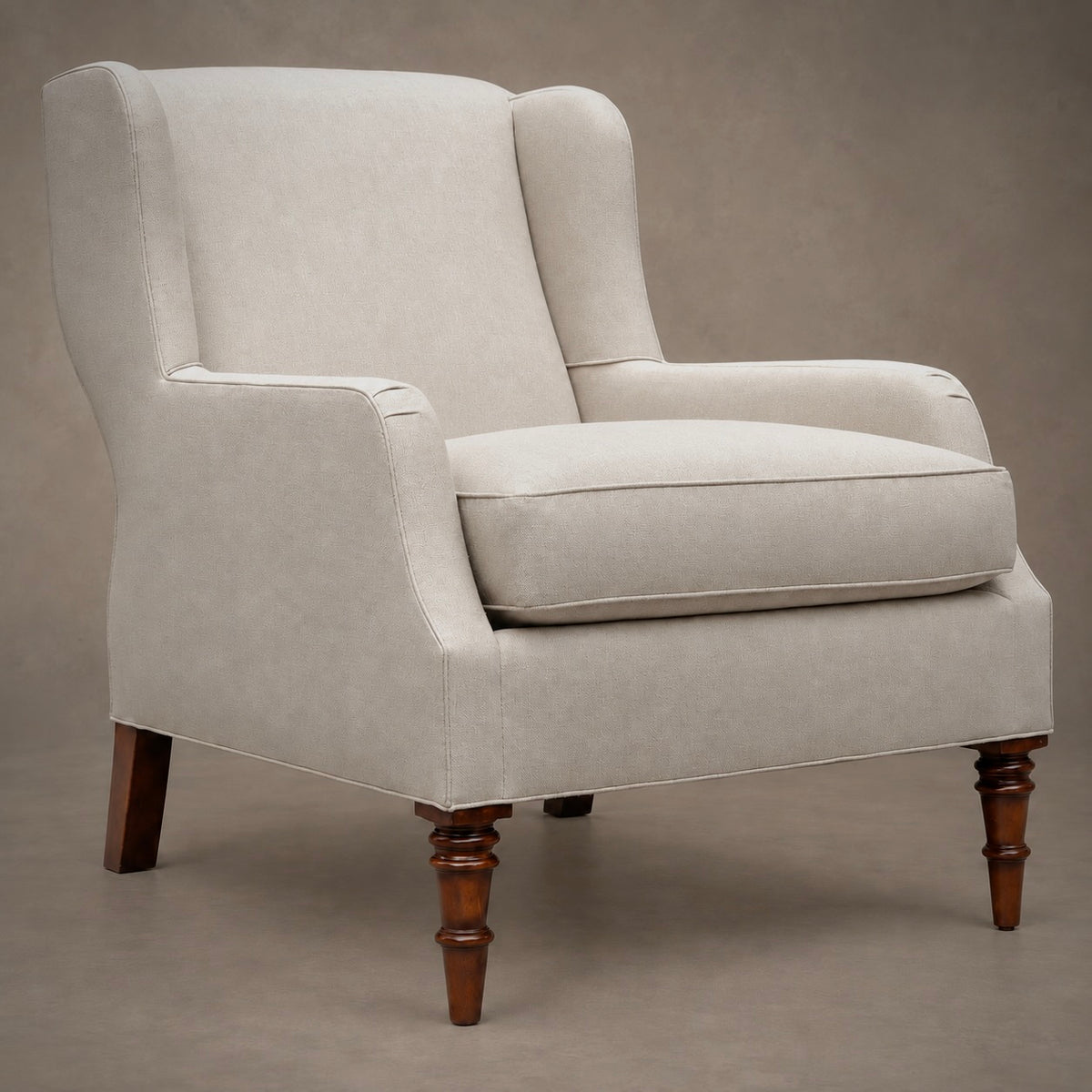 An upholstered wingback armchair in a light beige fabric with dark brown turned wooden legs, shown against a neutral studio backdrop.