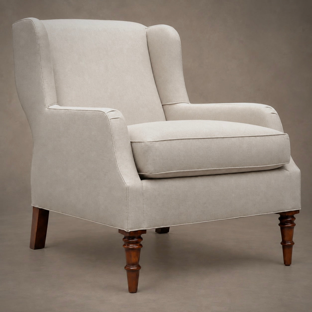 An upholstered wingback armchair in a light beige fabric with dark brown turned wooden legs, shown against a neutral studio backdrop.