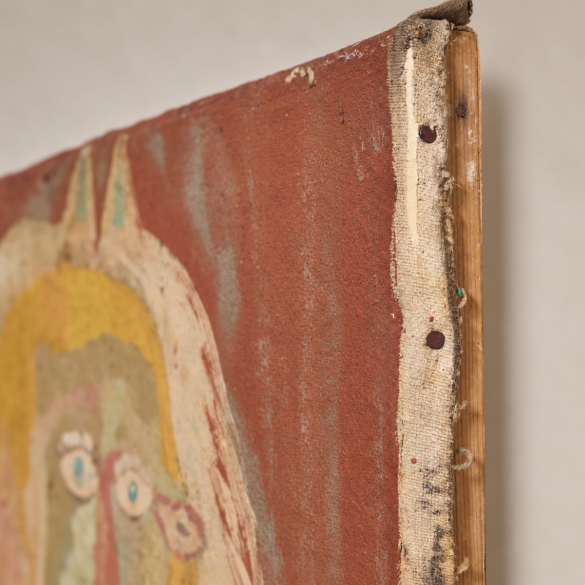 Close-up of the corner of a textured canvas painting showing the wooden frame edge, canvas backing, and painted surface in rust red, cream, and muted yellow tones.