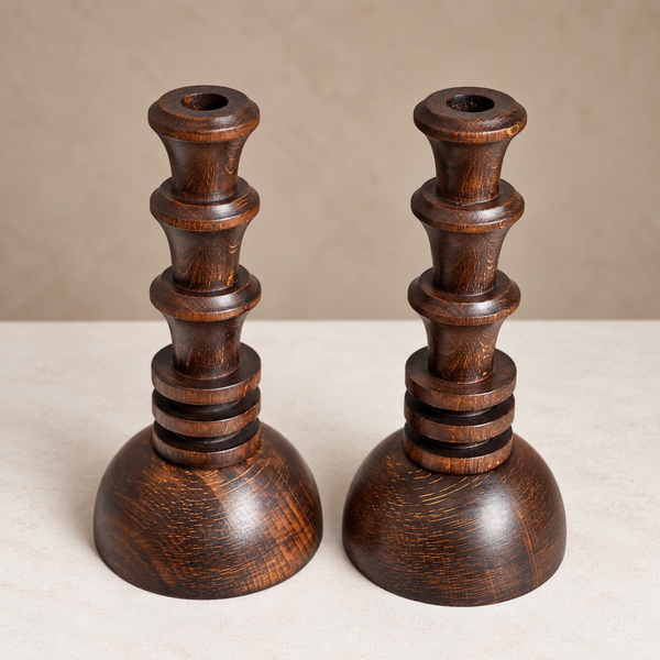A pair of dark brown wooden candlesticks with a stacked, tiered design and a rounded base, shown on a neutral beige background.