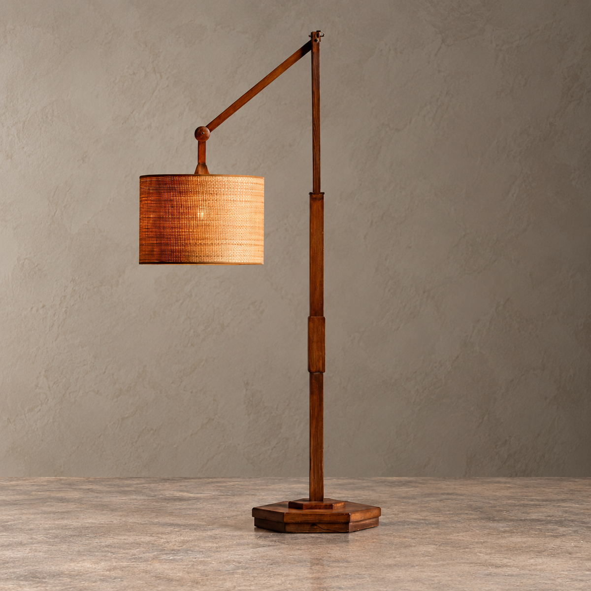 A modern wooden floor lamp with a hexagonal base, vertical pole, articulated arm, and a cylindrical woven shade, shown on a textured gray floor against a gray wall.