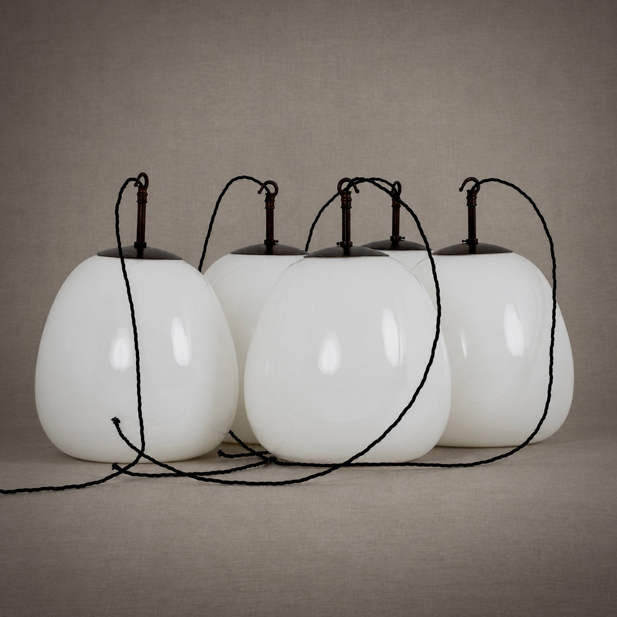 Four white teardrop-shaped pendant lights with black hanging cords, arranged in a row against a neutral textured beige background.