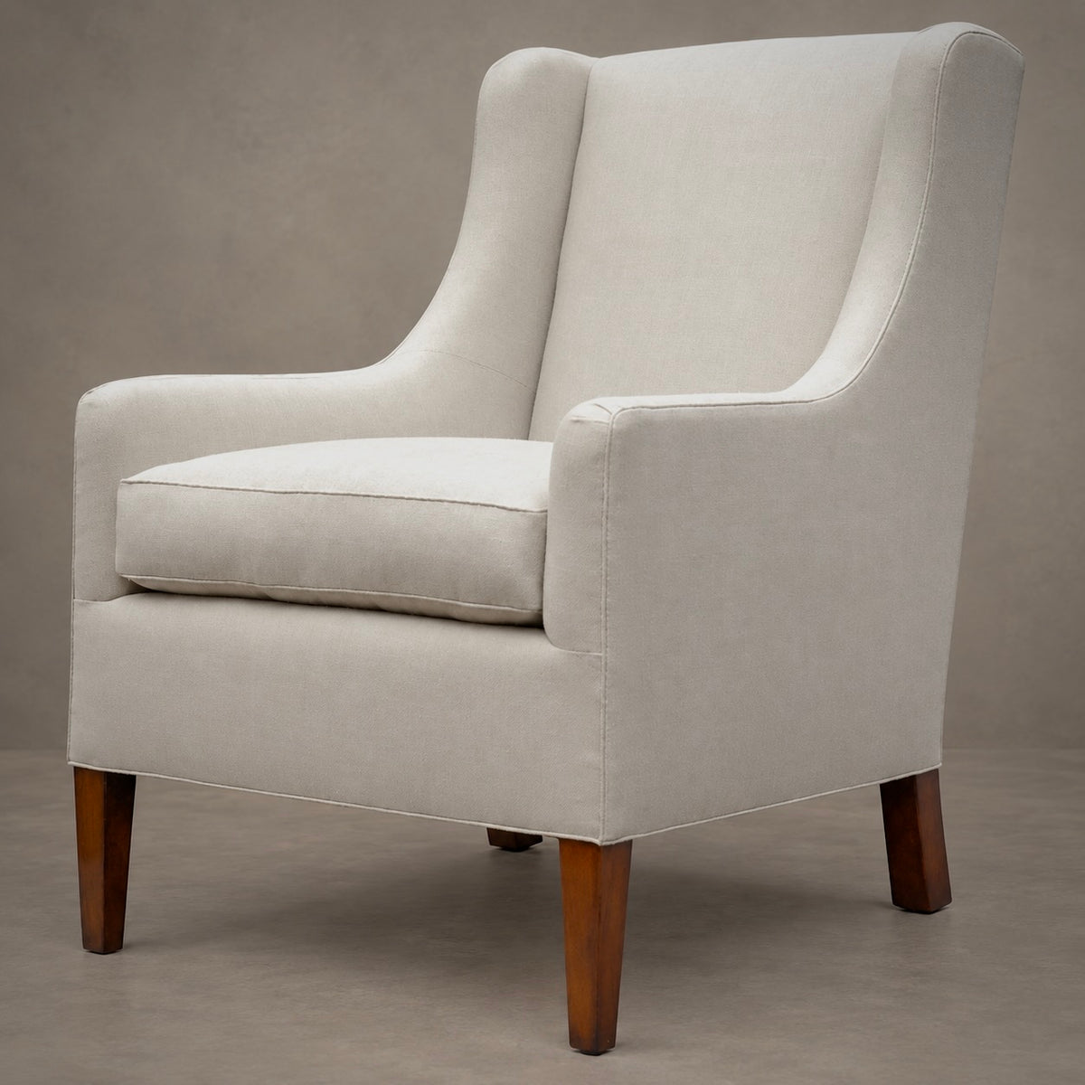 An upholstered wingback armchair in a light beige fabric with dark brown wooden legs, photographed against a neutral textured gray studio background.