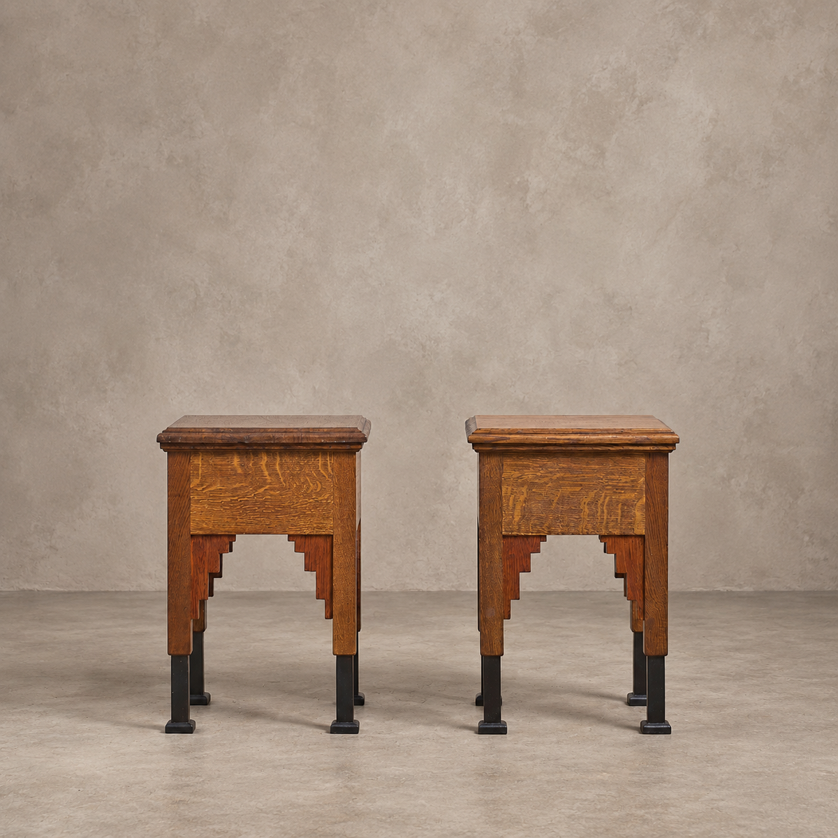 A pair of vintage wooden side tables with dark metal legs, set against a textured beige wall and concrete floor.
