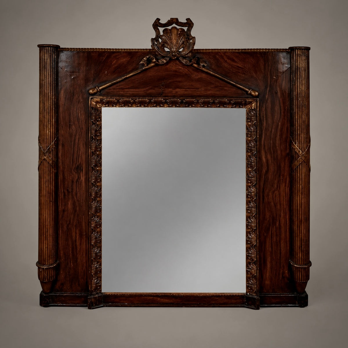 An early French mirror with carved and gilt wood, painted faux bois accents, reeded columns with conical finial bases, and a palmette motif gracing the border. A detailed carved shell crowns the pediment.