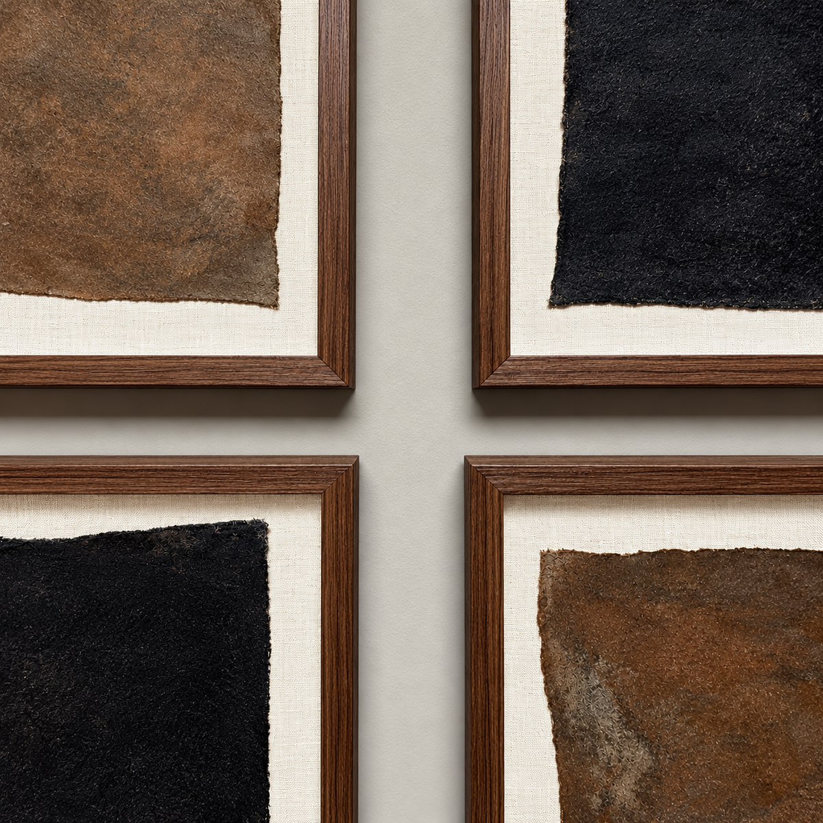 Four framed abstract art prints arranged in a 2x2 grid on a light gray wall. Each print features a textured square canvas in brown, black, or bronze tones with a cream mat and a dark wood frame.