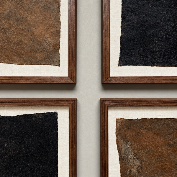 Four framed abstract art prints arranged in a 2x2 grid on a light gray wall. Each print features a textured square canvas in brown, black, or bronze tones with a cream mat and a dark wood frame.