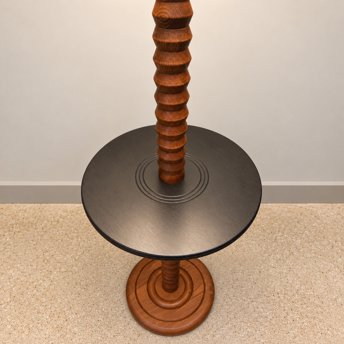 A round side table with a dark gray metal top and a carved reddish-brown wooden pedestal base and matching central column, photographed indoors against a plain wall and carpet.