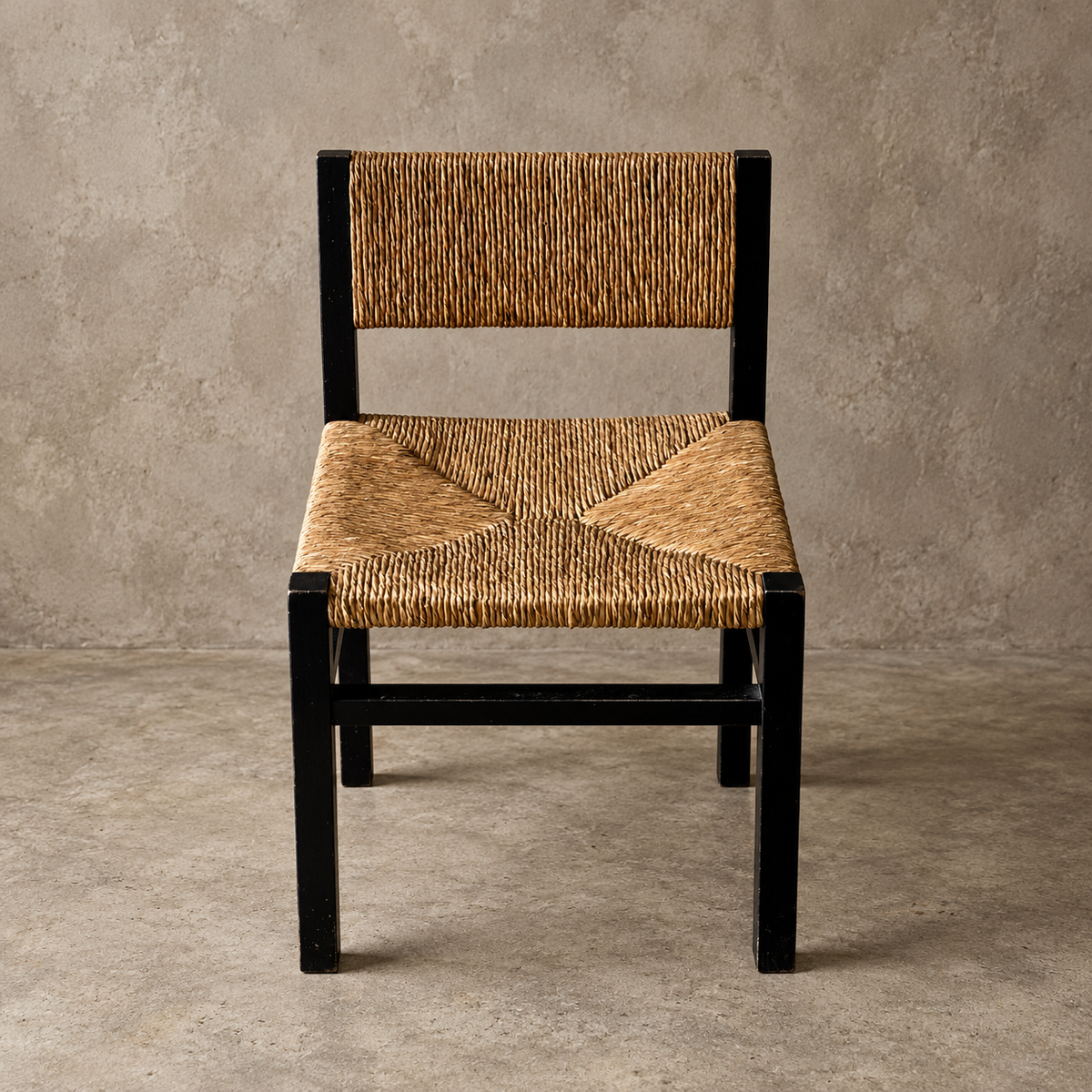Single chair with the black wood frame and a rush seat and back against a cement back