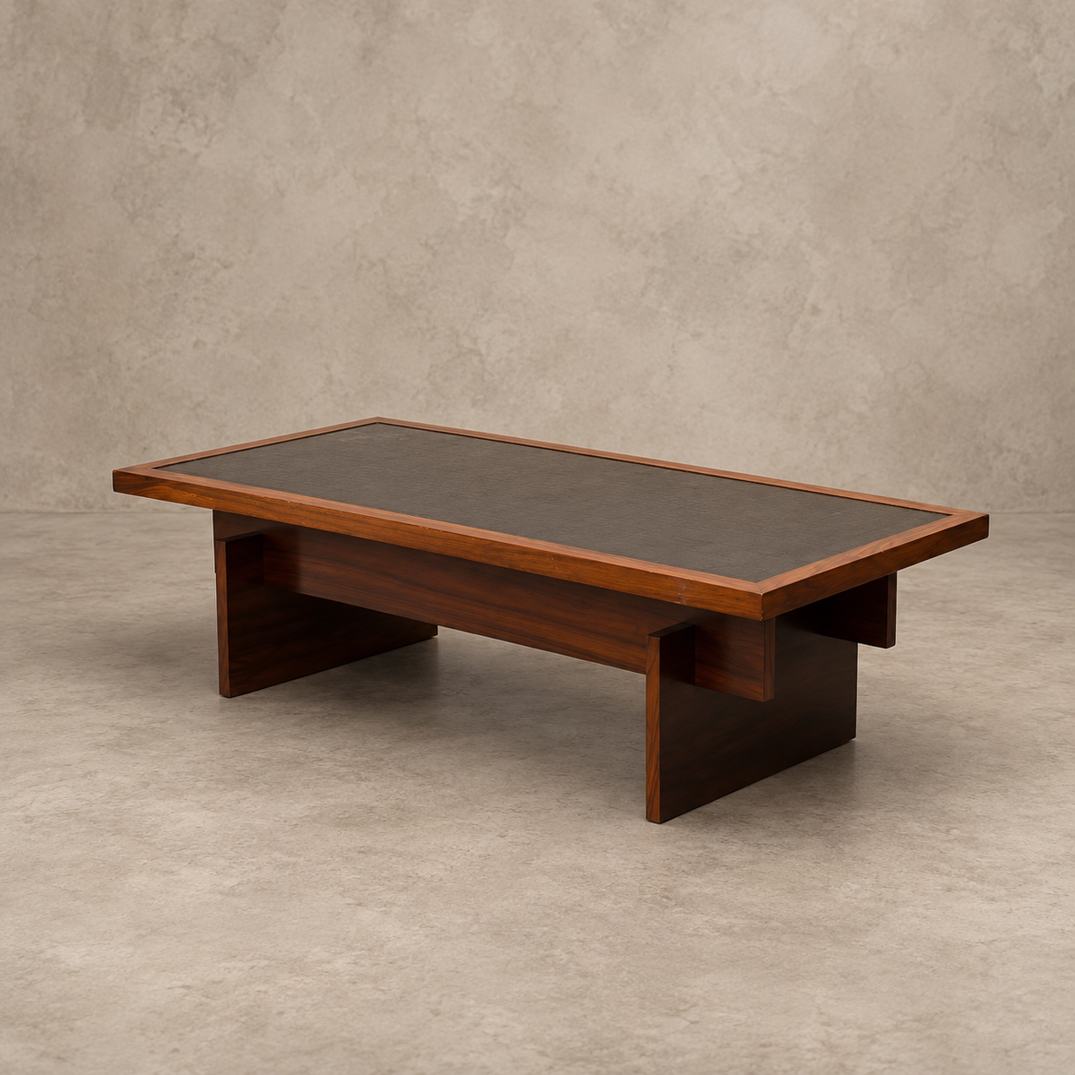 A mid-century modern rectangular coffee table with a dark wood frame, dark brown leather top, and open lower shelf, set against a textured beige concrete wall and floor.