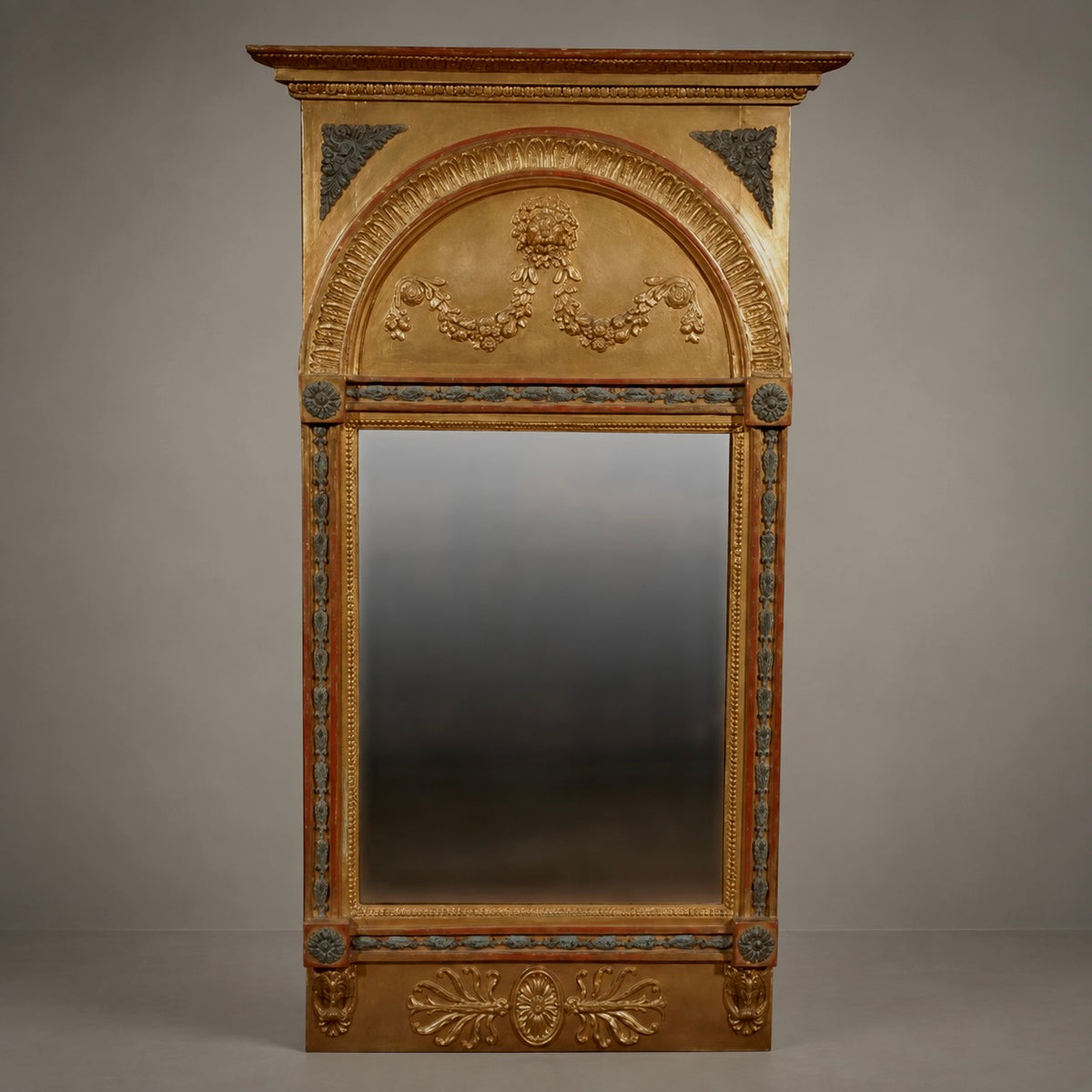 An ornate antique-style wall mirror with a gilded gold frame, featuring intricate floral carvings, decorative corner brackets, and a central mirror panel, set against a neutral gray background.