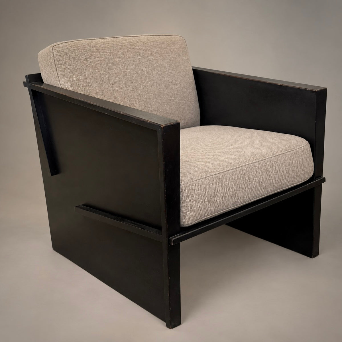 A modern armchair with a matte black wooden frame and light beige textured fabric cushions, photographed against a neutral gray studio background.
