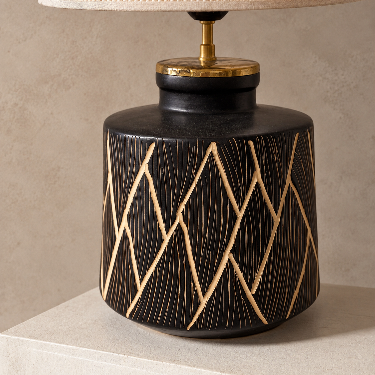 A ceramic table lamp with a black cylindrical base featuring a textured geometric pattern, topped with a beige fabric lampshade.