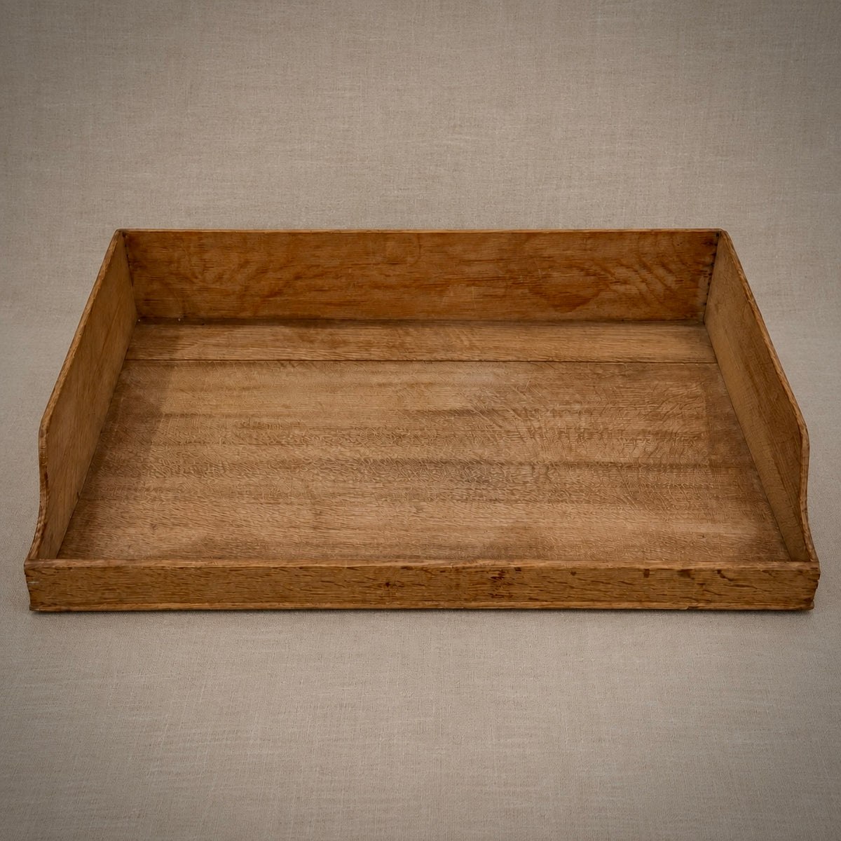 A rustic rectangular wooden tray with raised sides, shown from a top-down perspective on a textured beige fabric background.