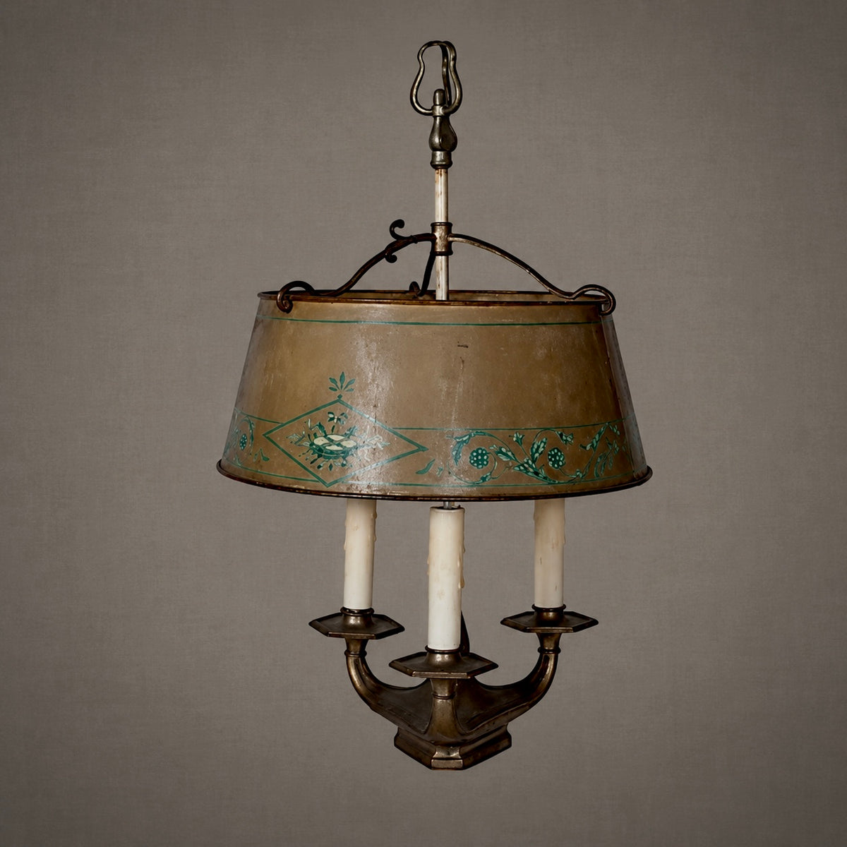 An antique three-light wall sconce featuring a bronze metal frame, a tapered bronze shade with green floral scrollwork, and three white candle-style bulbs.
