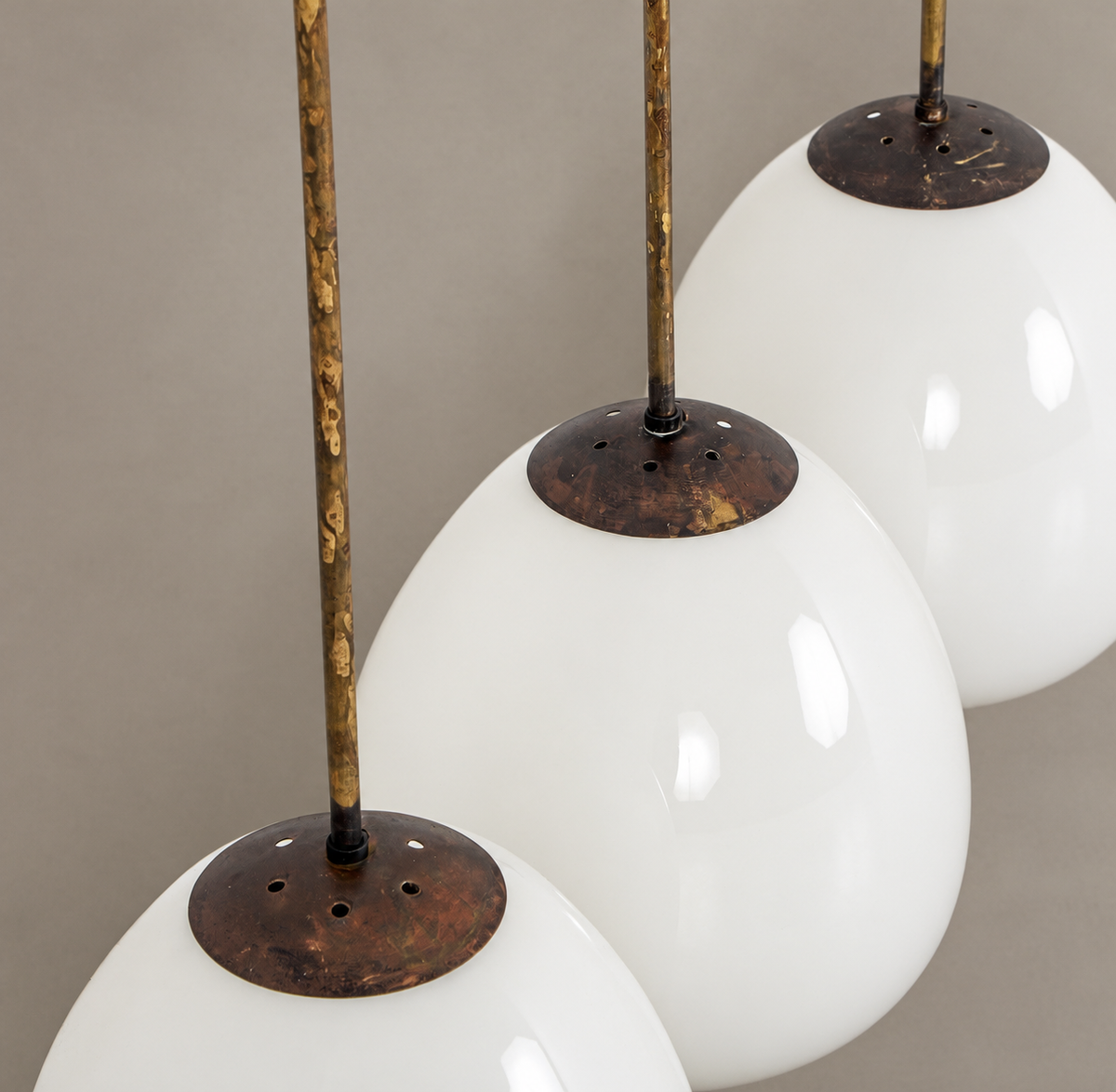 Three white glass pendant shades hanging from distressed bronze-finished rods with matching round metal caps, shown against a neutral gray background.
