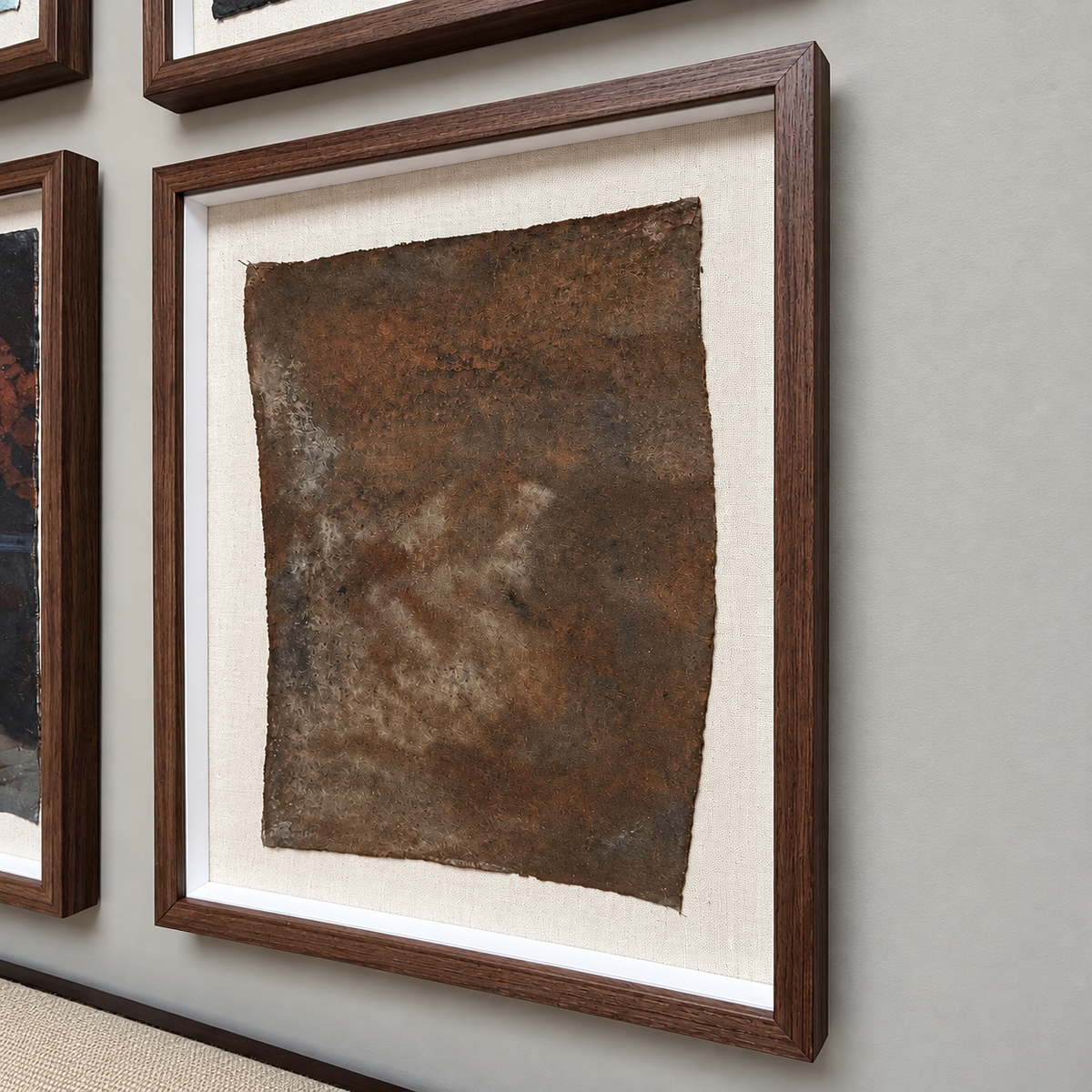 A framed abstract art print featuring a textured, rust-brown square on a cream mat, housed in a dark brown wooden frame and displayed on a light gray wall.