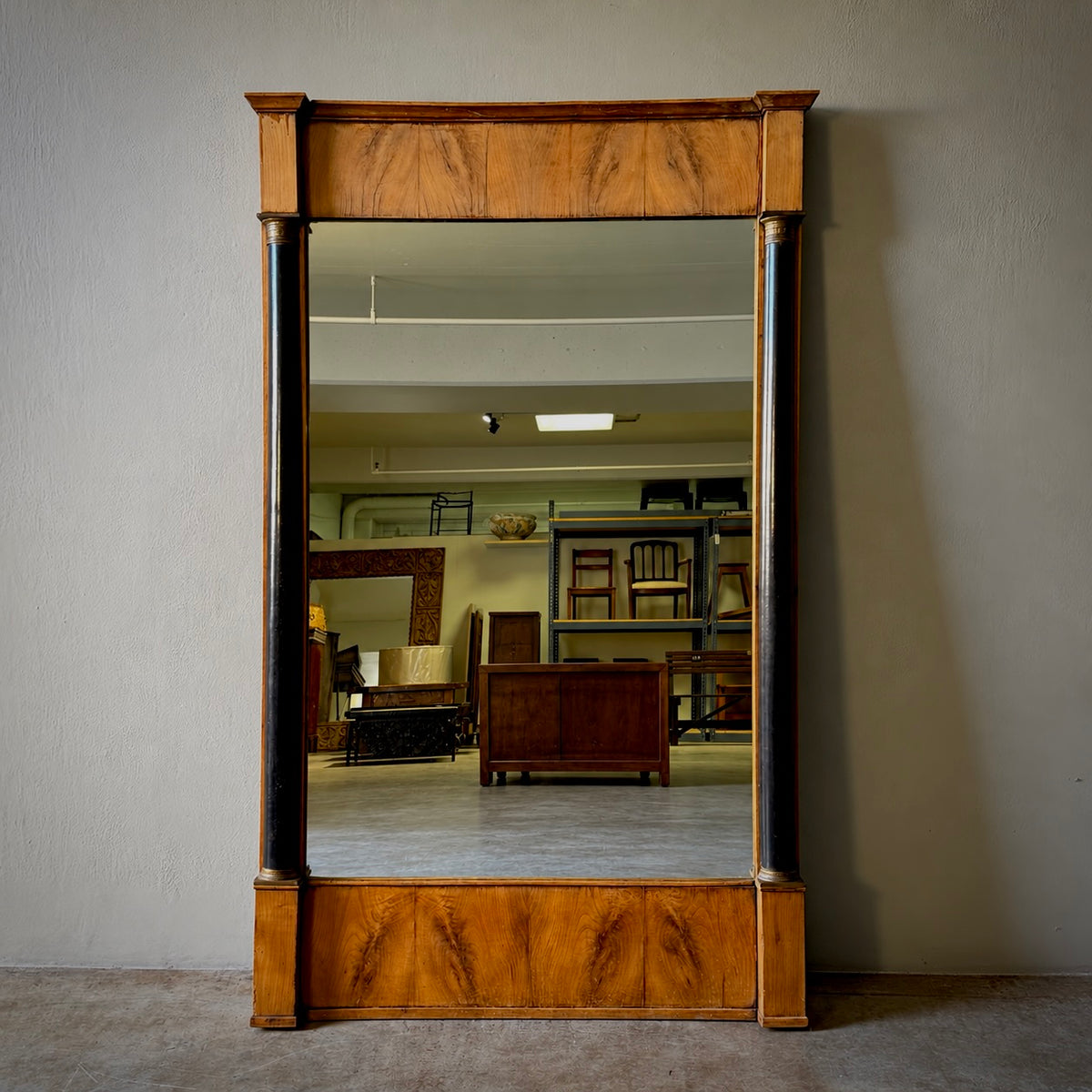 A large rectangular wall mirror with an ornate wooden frame, featuring dark vertical side panels and polished wood detailing at the top and bottom, set against a plain gray wall.