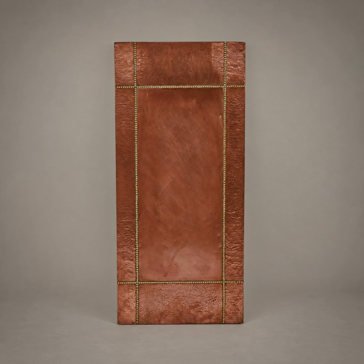 A rectangular copper wall art panel with a textured metallic finish, featuring a raised central panel and a decorative border accented with brass-toned nailhead trim, shown against a neutral gray background.