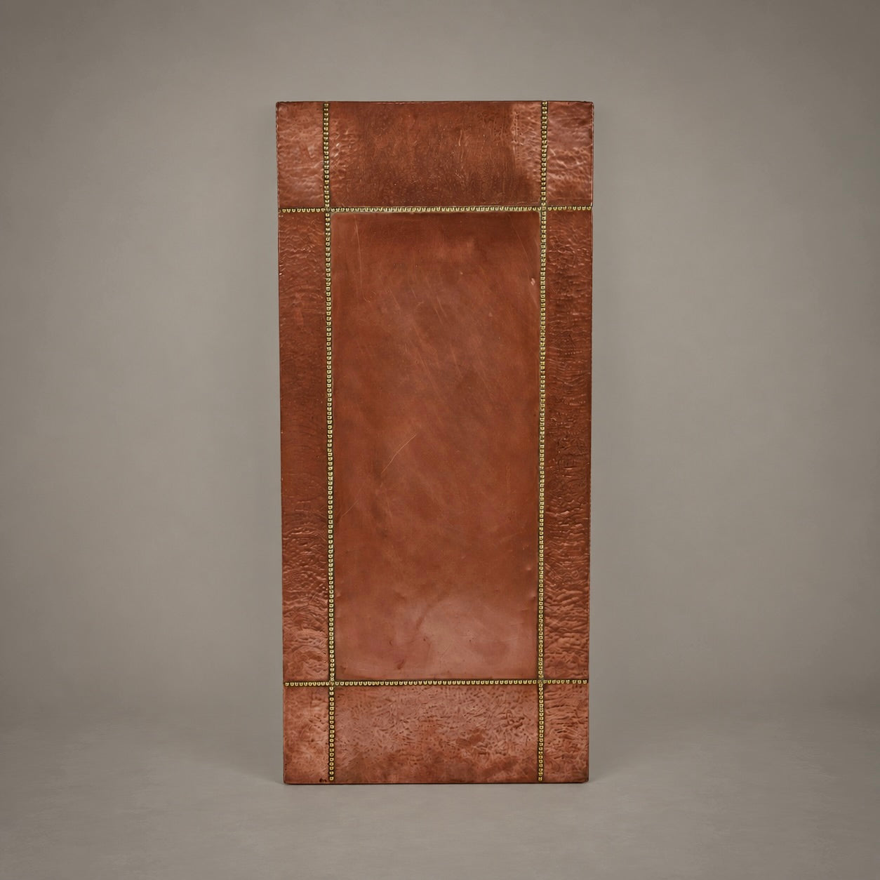 A rectangular copper wall art panel with a textured metallic finish, featuring a raised central panel and a decorative border accented with brass-toned nailhead trim, shown against a neutral gray background.