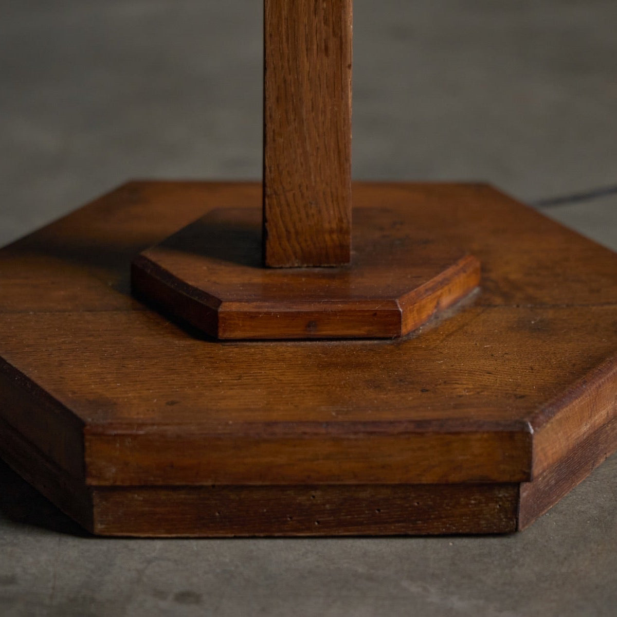 A close-up of a dark brown wooden lamp base with a hexagonal bottom and a vertical stem, photographed against a neutral gray background.