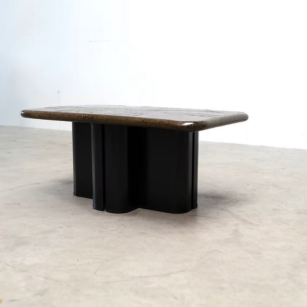 A mid-century modern low coffee table with a dark brown wood top and a black metal base, photographed in a minimalist studio setting with a concrete floor and white wall.