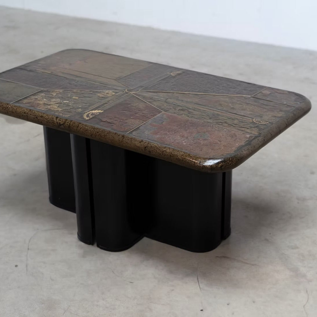 A mid-century modern coffee table with a dark brown and black tiled top and a black block base, photographed on a concrete floor against a white wall.