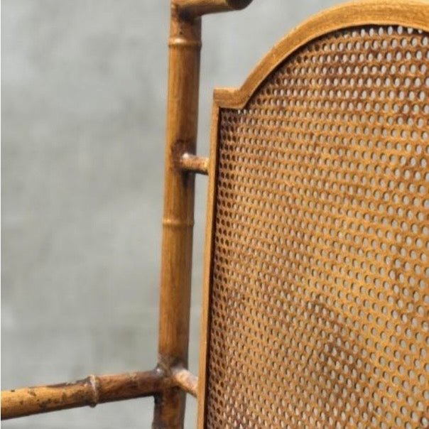 Close-up of a rustic bamboo chair frame with a woven cane backrest, showing the natural wood joints and texture against a neutral gray background.