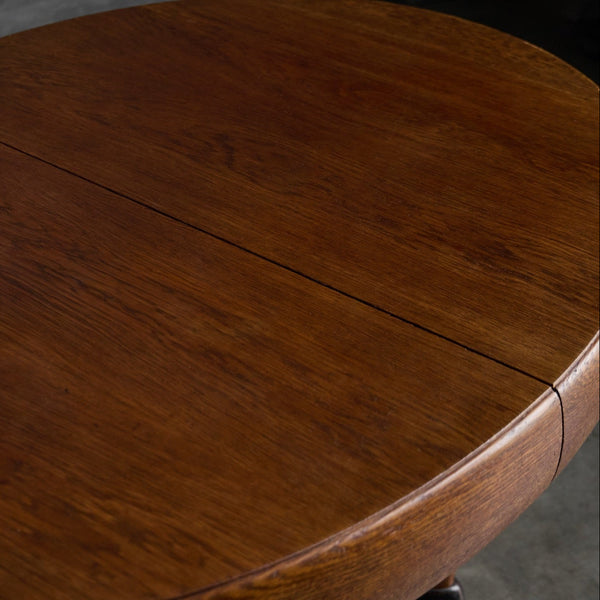 Close-up of a round wooden table with a warm medium-brown finish and visible wood grain, showing a center seam and part of the curved edge.