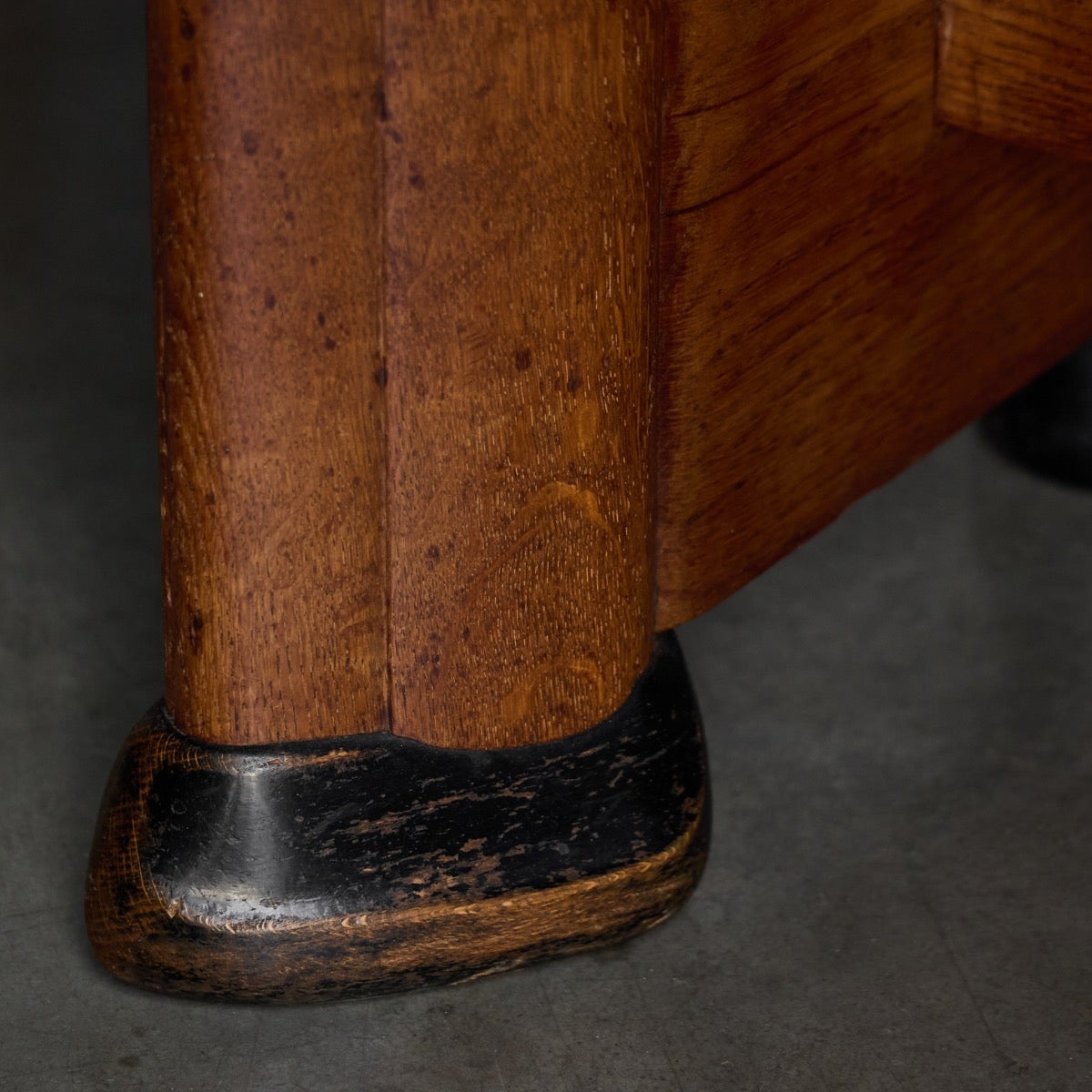 Close-up of a wooden table leg with a dark black metal cap on a gray concrete floor.