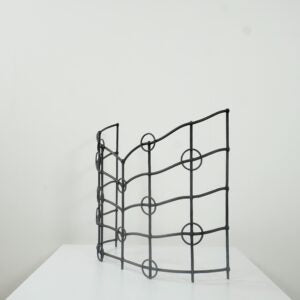 A black metal wire decorative screen panel with a wavy top edge and circular geometric patterns, displayed on a white surface against a plain white wall.